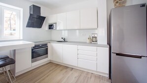 A modern kitchen with white cabinets, a stainless steel refrigerator, a microwave, and a built-in oven. - Villa Vito (Bibinje)