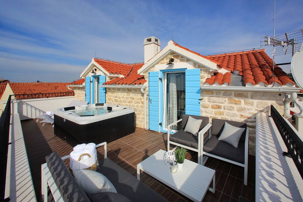 A rooftop terrace with a hot tub, outdoor seating, and a stone wall.