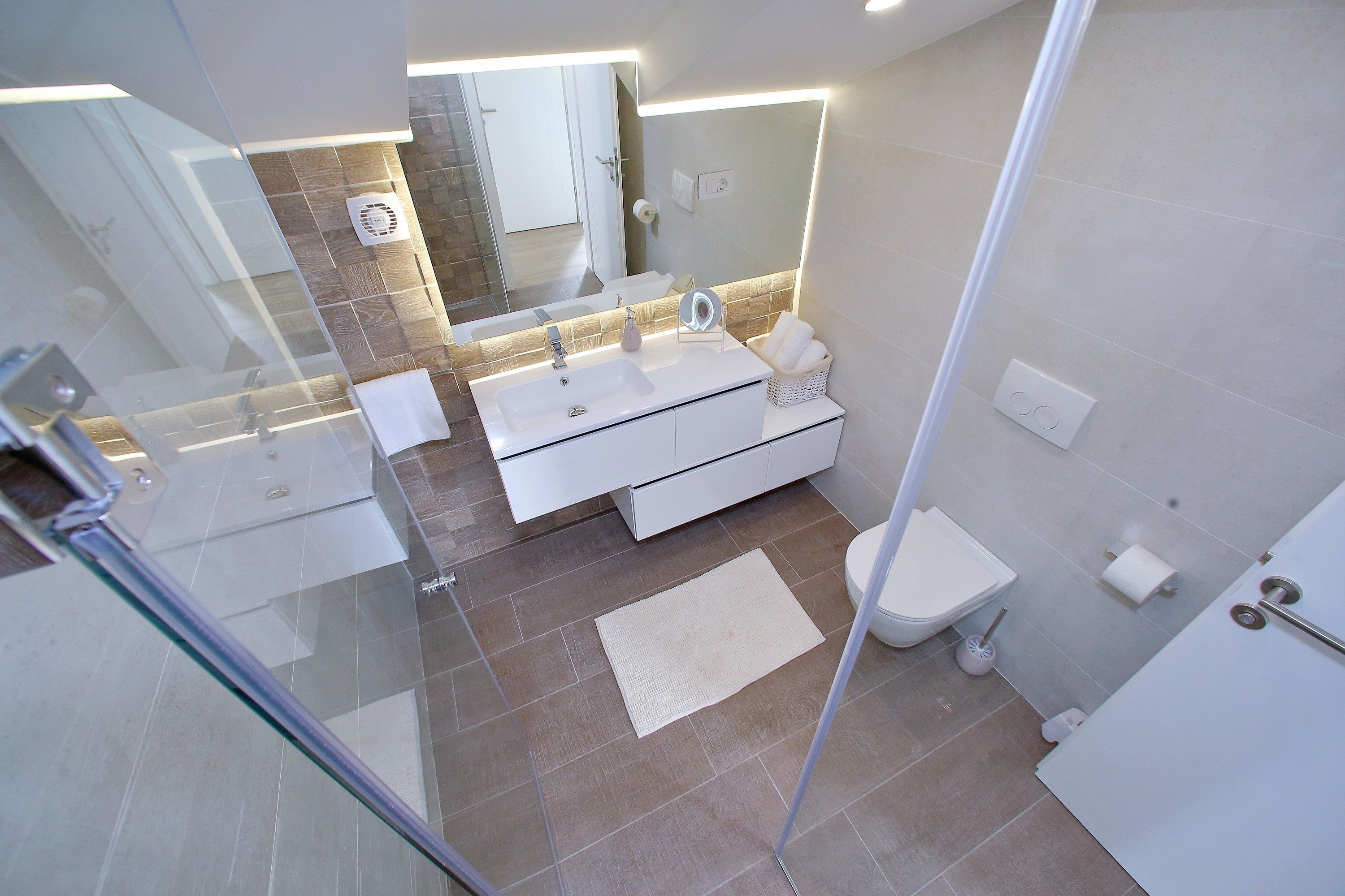Une salle de bain moderne avec une douche à parois de verre, un meuble-lavabo blanc avec un miroir et des toilettes.