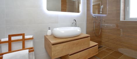 A modern bathroom with a white sink, wooden vanity, and a mirror with integrated lighting.