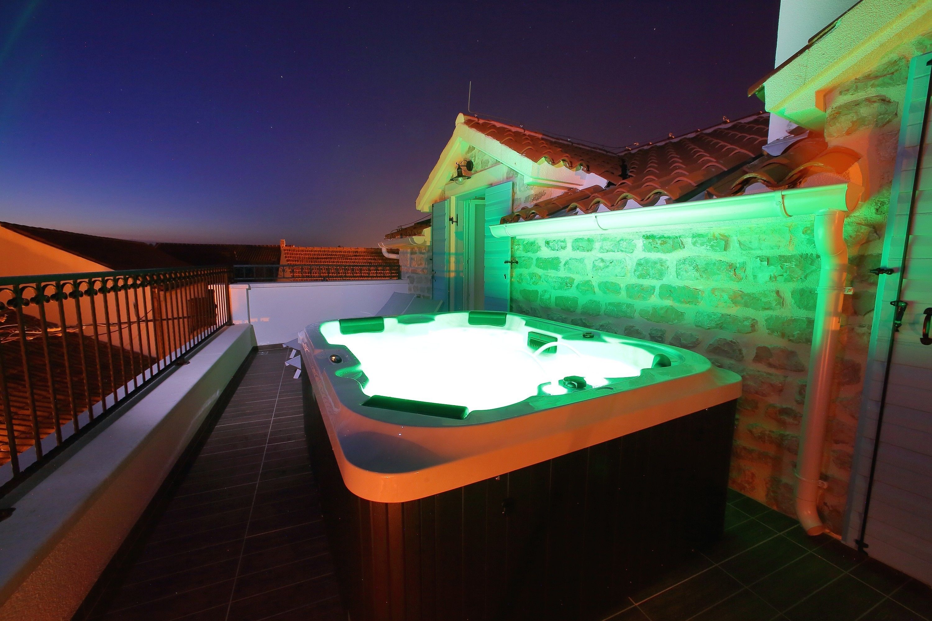 A hot tub on a balcony with a stone wall and a tiled roof.
