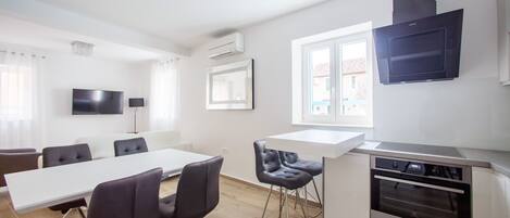 A modern kitchen with a built-in oven, a dining area with a long table and chairs, and a TV mounted on the wall.