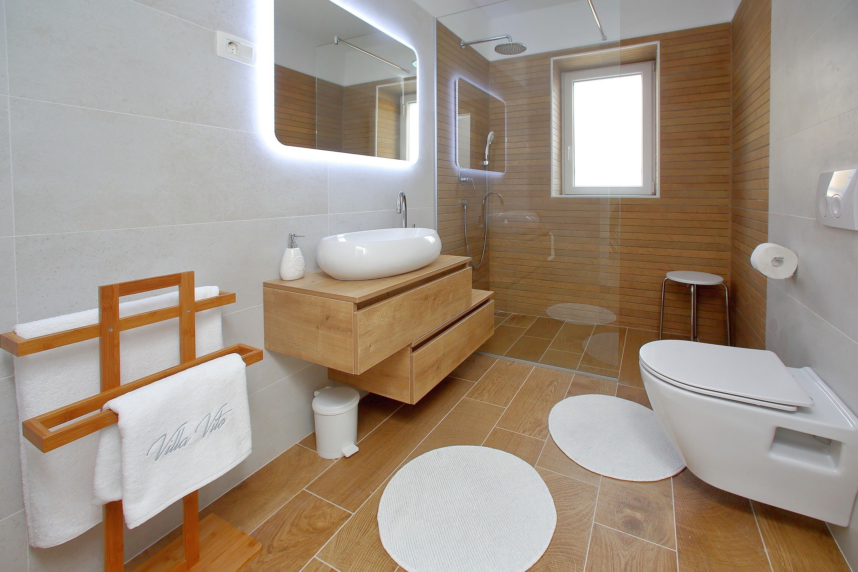 Een moderne badkamer met een houten wastafelmeubel, een witte wasbak, een toilet en een douchehoek.