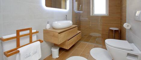 Een moderne badkamer met een houten wastafelmeubel, een witte wasbak, een toilet en een douchehoek.