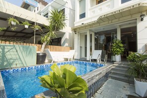 A swimming pool with a tiled edge, surrounded by potted plants and white lounge chairs.