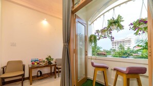 Une pièce dotée d’une porte-fenêtre coulissante, d’une petite table avec une plante, de deux chaises et d’une vue sur un immeuble par la fenêtre.