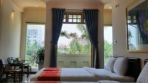 Une chambre d’hôtel avec deux lits, un ventilateur de plafond, un appareil de climatisation, un bureau avec des chaises et une grande fenêtre avec des rideaux.