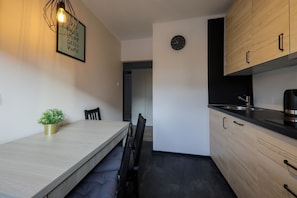 A modern kitchen with wooden cabinets, a black countertop, and a dining area with a bench and chairs. - RentPlanet - Apartament Kościelna (Zakopane)
