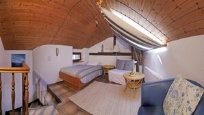 A cozy bedroom with a wooden ceiling, a bed, a blue sofa, a small round table, and a window with a view. - Hotel Saarburger Hof (Saarburg)