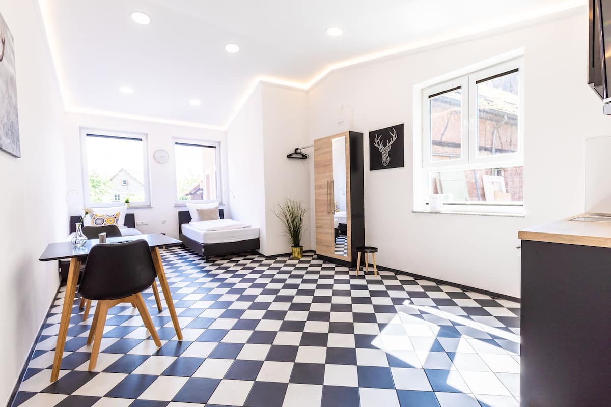 Une chambre moderne avec un sol à carreaux, un lit, un bureau et une fenêtre donnant sur une maison.