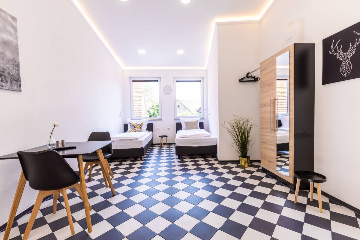 Une chambre moderne avec un sol à carreaux, deux lits, une table à manger avec des chaises et un grand miroir.