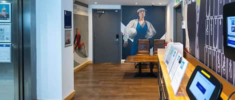 A hotel lobby with a reception desk, a large poster of a woman in a blue dress, and a sign indicating the direction to the bedrooms.