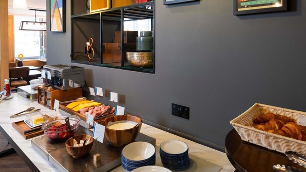 A buffet setup with various food items and a wall with framed pictures. - ibis budget Swindon Town Centre (Swindon)