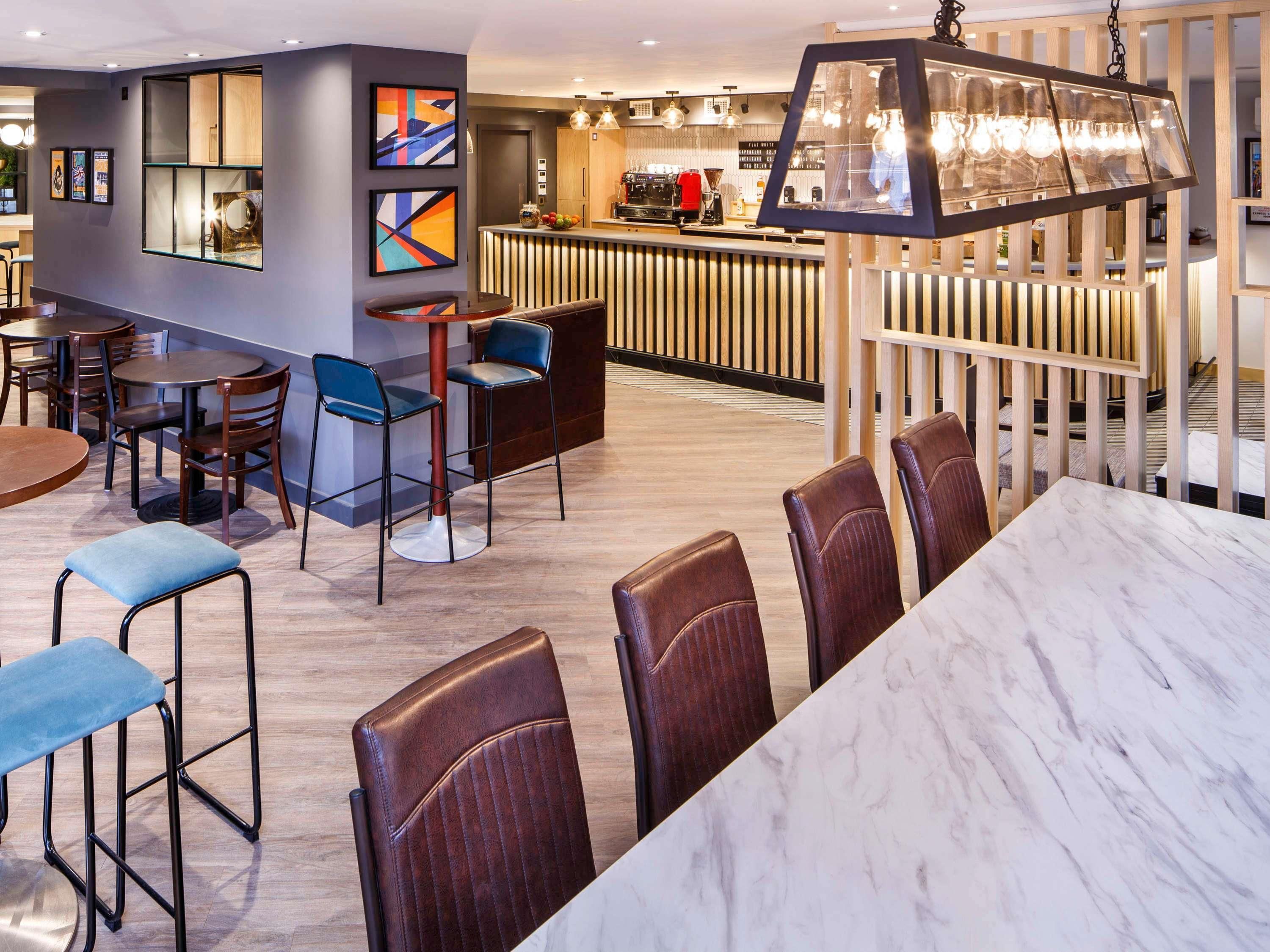 A modern restaurant with a bar area, seating arrangements, and a decorative light fixture.