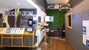 A reception area with a desk, seating, a green wall, and a TV screen. - ibis budget Swindon Town Centre (Swindon)