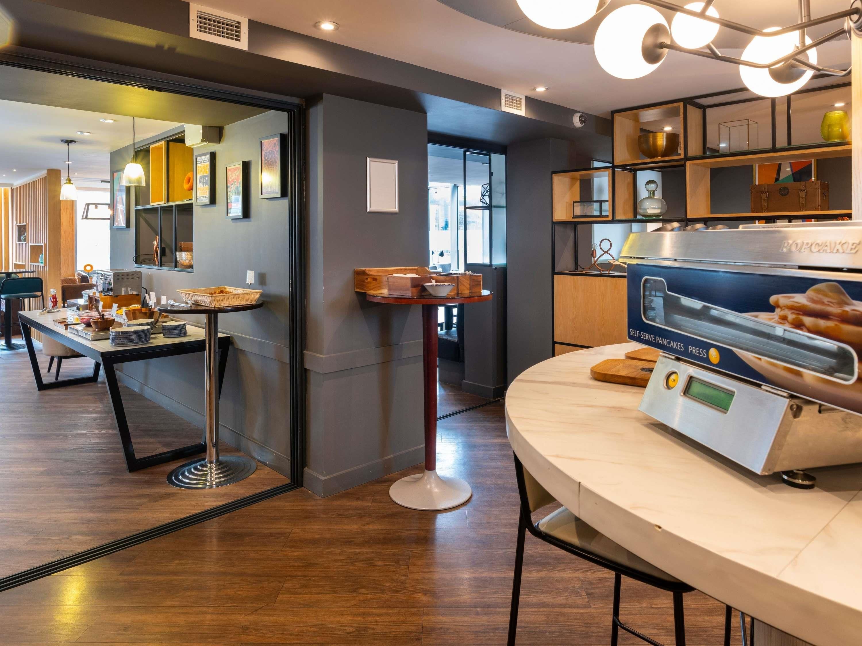 Una cocina moderna con una máquina para hacer panqueques, estantes de madera con utensilios de cocina, y un comedor con mesa y sillas.