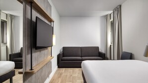 Habitación de hotel con cama, sofá, televisión y suelo de madera.