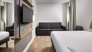 Habitación de hotel con cama, sofá, televisión y suelo de madera.