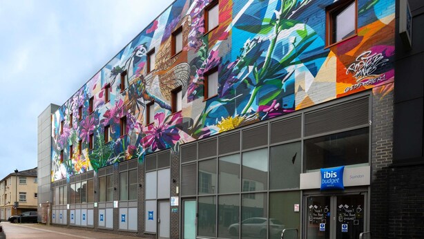 Un edificio con un mural colorido, ventanas amplias y un cartel de ibis budget hoteles.