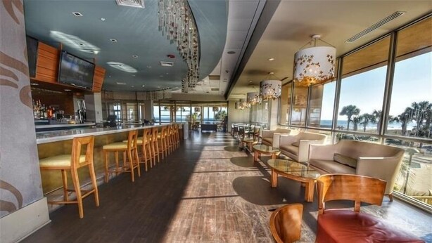 A spacious bar area with wooden chairs and tables, large windows offering a view, and a modern ceiling design. - 110 South Hampton - Barefoot Resort Rentals (Myrtle Beach)