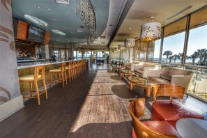Um espaço de bar amplo, com cadeiras e mesas de madeira, grandes janelas com vista e um design moderno no teto.