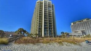 A tall hotel with multiple floors and balconies, located near a beach with a sandy path leading to the entrance. - 110 South Hampton - Barefoot Resort Rentals (Myrtle Beach)