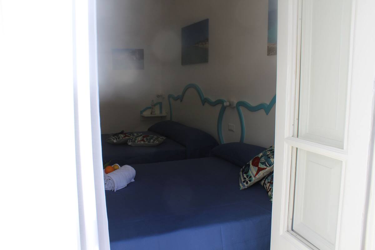 Een kamer met twee bedden, een klein tafeltje en een wandplank.