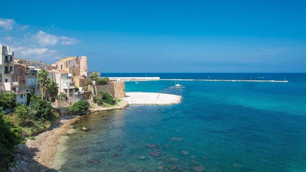 A coastal town with buildings along the shore, a clear blue sea, and a pier extending into the water. - Exclusive Home (Castellammare del Golfo)