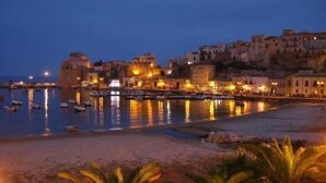 A coastal town at dusk with buildings along the waterfront and boats in the water. - Exclusive Home (Castellammare del Golfo)