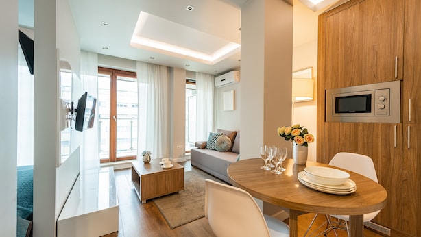 Una sala de estar moderna con un sofá, una mesa de comedor con sillas, un televisor de pantalla plana en la pared y un mueble de madera.
