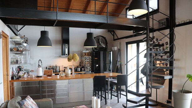 A modern kitchen with a central island, a dining area with chairs, a staircase, and a living room with a sofa and a coffee table. - Skylark Bed & Breakfast (Grasse)