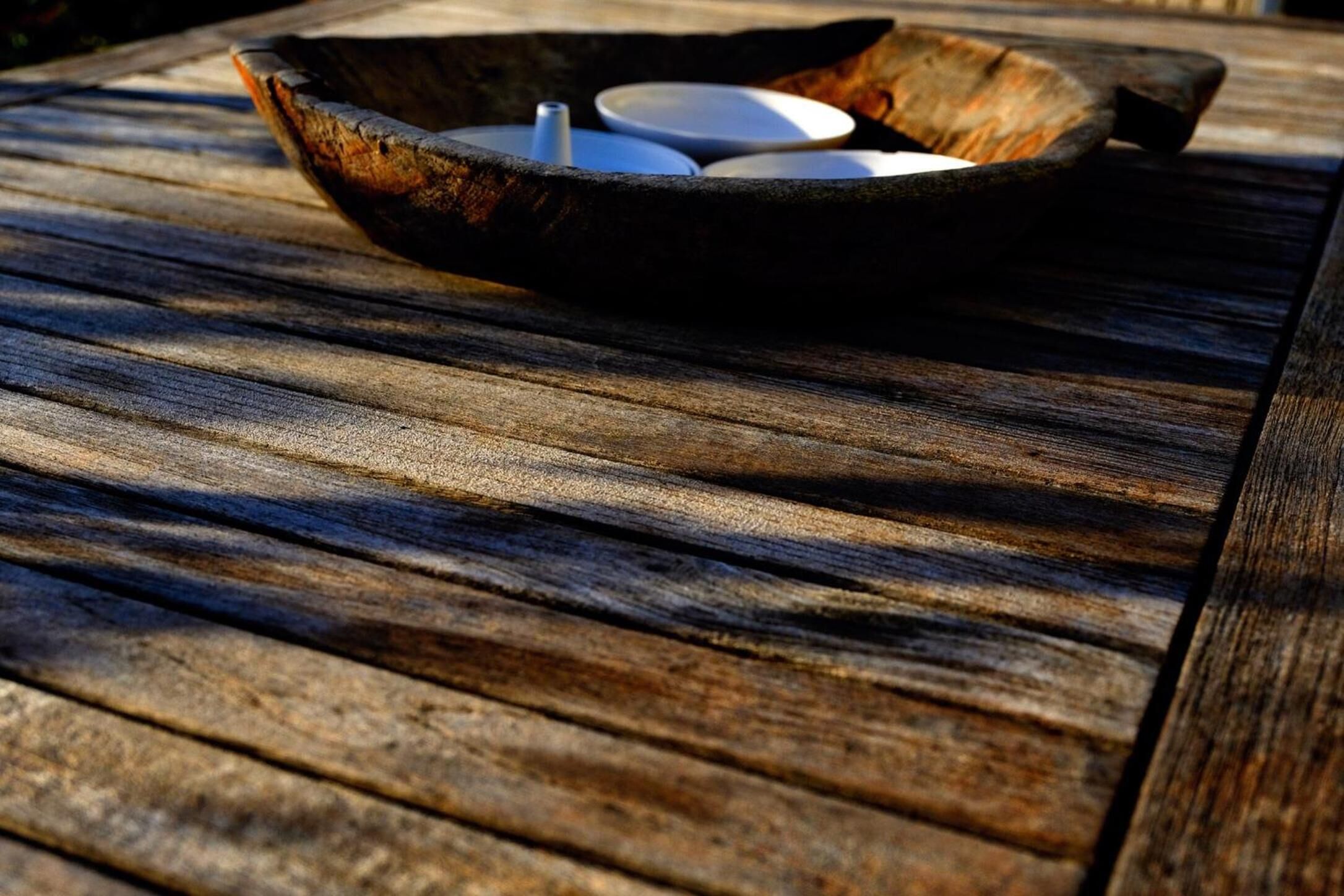 A rustic wooden table with a metal bowl containing white cups and a spoon.