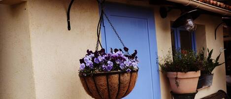 Una puerta azul adornada con una cesta de flores colgante, un banco y macetas con plantas a la derecha.