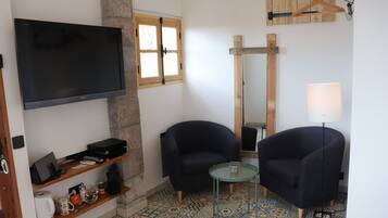 A living room with a flat-screen TV, two armchairs, a small round table, a lamp, and a patterned floor.