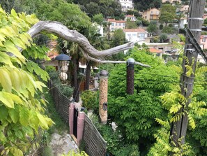 A lush garden with a large tree, a metal fence, and a stone structure.