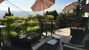 An outdoor patio area with multiple tables and chairs, surrounded by greenery and overlooking a scenic view. - Skylark Bed & Breakfast (Grasse)