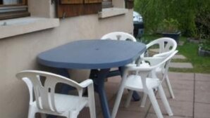 Un patio con una mesa redonda y cuatro sillas de plástico blancas.