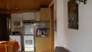 Cocina compacta con refrigerador, estufa y microondas. Hay una mesa de comedor con sillas y un sofá en la sala.
