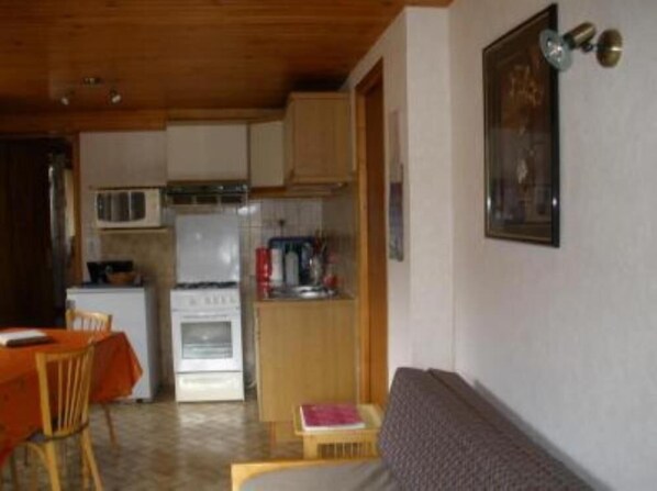 Cocina compacta con refrigerador, estufa y microondas. Hay una mesa de comedor con sillas y un sofá en la sala.