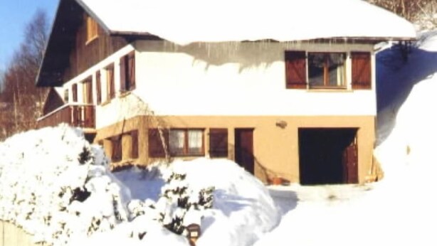 Una cabaña de dos pisos con techo nevado y un amplio porche delantero.