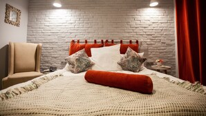 Un dormitorio con pared de ladrillo, una cama con ropa de cama roja y blanca, una silla y una mesita con una planta.