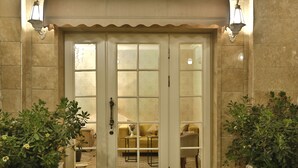 Una entrada con doble puerta que ofrece vista a un espacio con sofá y una mesita. Hay plantas en macetas a cada lado de la puerta.