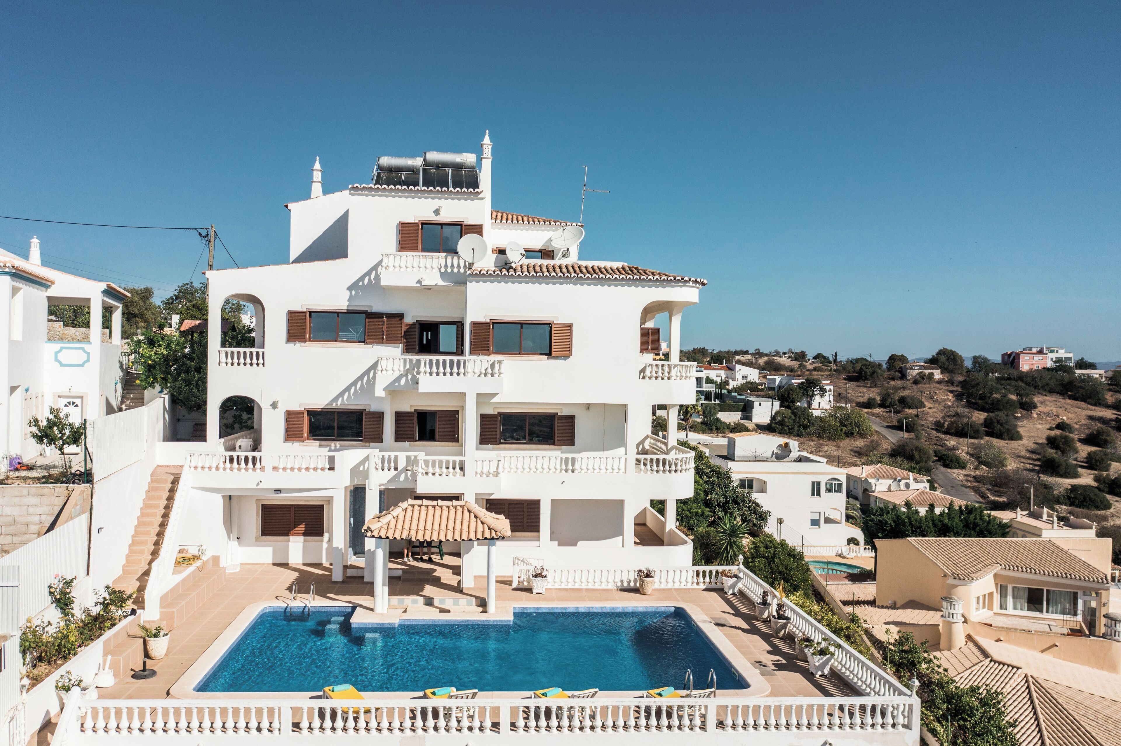 Un immeuble blanc à plusieurs étages, doté d’une piscine, de balcons et offrant une vue sur le paysage environnant.