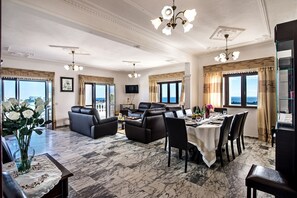 Uma sala de estar espaçosa com lareira, uma área de jantar com mesa posta para quatro pessoas e grandes janelas com vista para a cidade.