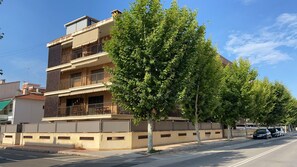 Un edificio residencial de varios pisos con balcones, un acceso con portón y árboles a lo largo de la calle.