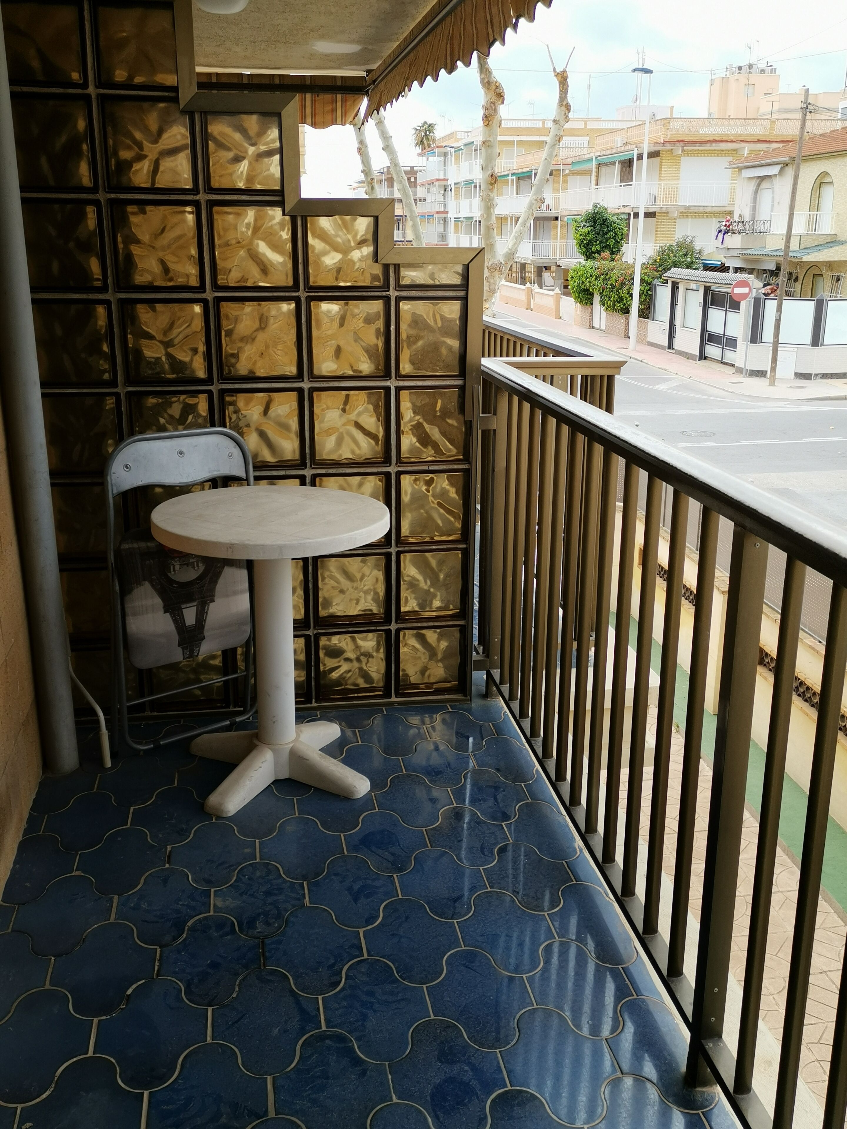 Un balcón con piso estampado, una mesa redonda pequeña y una silla.