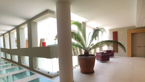 A spacious indoor area with a large potted plant, a pool, and a red seating area. - Bilocale Marina (Gallipoli)