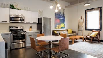 A modern kitchen with stainless steel appliances, a dining area with a round table and chairs, and a living space with a sofa and a window.