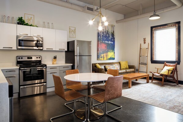 A modern kitchen with stainless steel appliances, a dining area with a round table and chairs, and a living space with a sofa and a window. - Hotel Clemons (Chattanooga)
