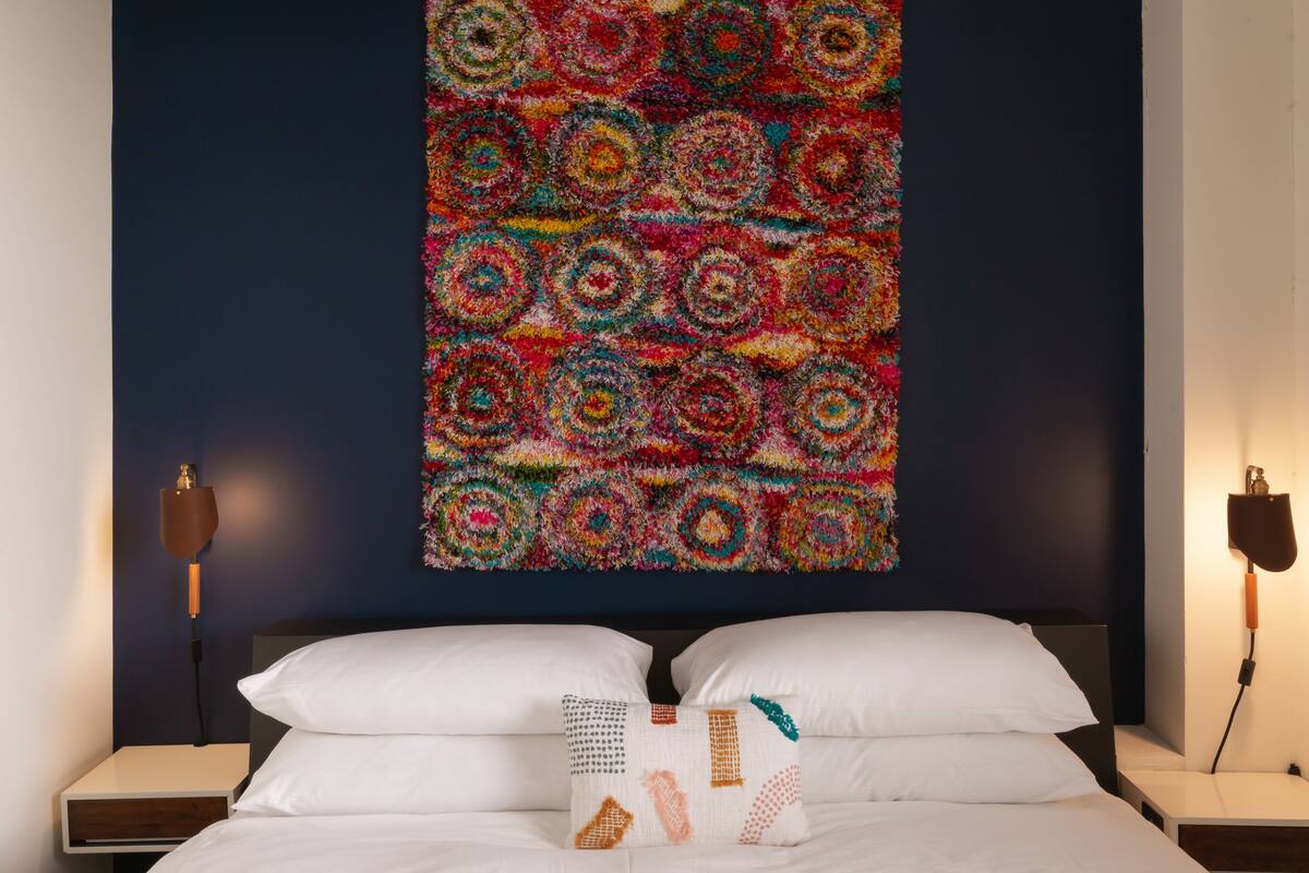 A bedroom with a bed, two bedside tables, and a colorful wall hanging.